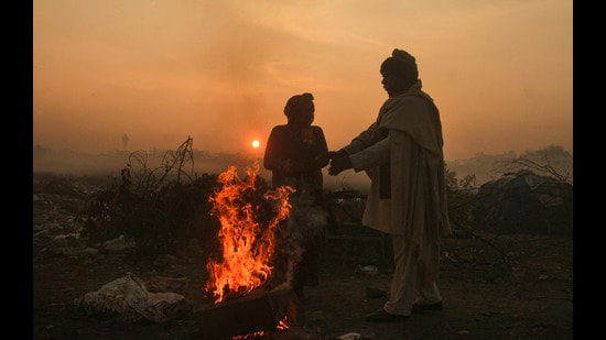 People stand near a small fire to warm themselves during a cold winter morning in Gurugram on Friday. (PTI)
