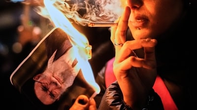 A protester smokes a cigarette after lighting it off a burning poster of Iran's Supreme Leader Ayatollah Ali Khamenei during a demonstration in Berlin, Germany (AP) A protester smokes a cigarette after lighting it off a burning poster of Iran's Supreme Leader Ayatollah Ali Khamenei during a demonstration in Berlin, Germany (AP)