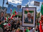An unidentified man holds a picture of Reza Pahlavi while members of the Iranian community and supporters hold signs and pre-regime Iranian flags during a "Solidarity with the People of Iran" event in front of City Hall in Downtown 