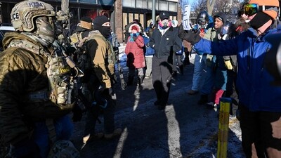Federal agents (L) look on as demonstators gather near the site of where state and local authorities say a man was shot by federal agents earlier in the morning in Minneapolis, Minnesota, on January 24, 2026. Minnesota Governor Tim Walz said Saturday that federal agents deployed in Minneapolis as part of a sweeping immigration crackdown had carried out "another horrific shooting," less than three weeks after the fatal shooting of Renee Good. (Photo by ROBERTO SCHMIDT / AFP) (AFP) Federal agents (L) look on as demonstators gather near the site of where state and local authorities say a man was shot by federal agents earlier in the morning in Minneapolis, Minnesota, on January 24, 2026. Minnesota Governor Tim Walz said Saturday that federal agents deployed in Minneapolis as part of a sweeping immigration crackdown had carried out "another horrific shooting," less than three weeks after the fatal shooting of Renee Good. (Photo by ROBERTO SCHMIDT / AFP) (AFP)