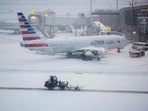 A snow removal machine is seen working while a Boeing 737 American Airlines passenger aircraft is parked at gate on the tarmac of LaGuardia airport.