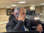 The image captures Netanyahu in a black jacket over a white shirt, standing beside a dark-coloured vehicle while speaking on his phone.