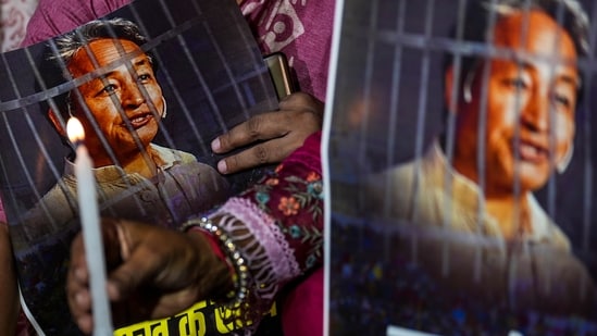 Agitators hold posters and a candle during a protest by AAP over the arrest of climate activist Sonam Wangchuk, at Jantar Mantar, in New Delhi. (PTI File)