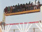 The clip shows the ride operating at high speed when one side of its supporting pillars suddenly collapses, causing the entire structure to tilt and crash to the ground.