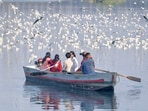 People feed birds from a boat in the Yamuna Bazaar area along the Yamuna River, enjoying the pleasant weather on the riverbank in New Delhi, India, 