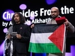 Director Abdallah Al-Khatib, left, addresses the audience after receiving the GWFF best first feature award for Chronicles from the Siege as Taqiyeddine Issaad, right, holds a Palestinian flag during the awards ceremony for the film festival in Berlin.