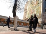Iranian women walk past a mural depicting a famous Persian miniature, painted on the side of a building block, in Tehran on February 22, 2026. 