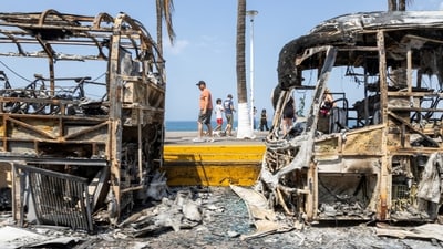 Tourists walk past the burnt wreckage of buses after a series of blockades and attacks by organized crime following the military operation in Jalisco. The killing triggered a wave of violent retaliation by the cartel, with vehicles and buses set ablaze across multiple states. (REUTERS)