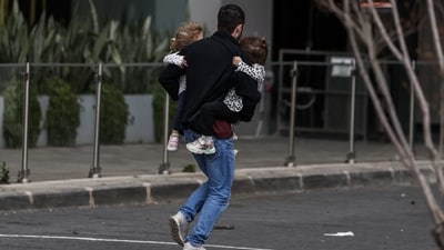 A man carries two children as he runs to take shelter after sirens sounded in Tel Aviv on February 28 after Israel launched attacks on Iran (AFP)