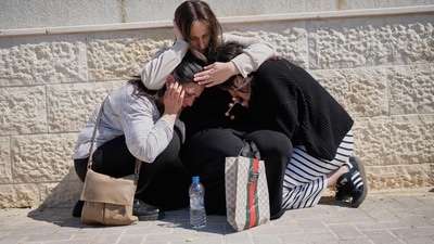 Mourners take cover while air-raid sirens warn of incoming missiles launched by Iran toward Israel during the funeral of Sarah Elimelech and her daughter Ronit who were killed in an Iranian missile attack, in Beit Shemesh, Israel, Monday, March 2, 2026. (AP Photo/Ohad Zwigenberg) (AP)