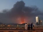Dubai Abu Dhabi news highlights: Foreign workers look at a tall plume of black smoke ascends following an explosion in the Fujairah industrial zone on March 3, 2026.