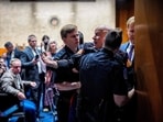 A protester dressed in a military uniform gets stuck in a door, injuring his arm, as Sen. Tim Sheehy attempts to remove him 