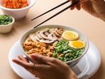 Adorable ceramic ramen bowls arranged on a wooden table, filled with noodles, greens, and rice, ready for a cosy meal.