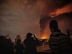 Residents look on and take pictures as flames and smoke rise from an oil storage facility struck as attacks hit the city during the U.S.–Israeli military campaign in Tehran, Iran.