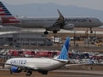 An American Airlines jetliner lands on a runway as a United Airlines plane waits for clearance to take off as high winds strafe Denver International Airport, in Denver.