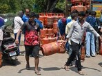 People carry a household LPG cylinder that they received after waiting in a long queue. People queued up to collect their household LPG cylinders amid an ongoing LPG shortage.