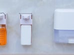 Adhesive bathroom accessories, including toothbrush holders, soap trays and towel rods, are neatly arranged on a tiled wall without drilling or permanent fixtures.