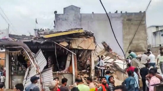 People gather after a four-storey building collapsed, trapping at least six persons in the debris, at Kotma town, in Anuppur district, (PTI)
