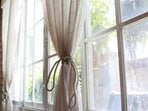 Soft summer curtains filter sunlight through the window, creating a cool, calm living space on warm afternoons at home.