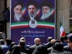 People sit before a banner depicting Iran's supreme leaders since 1979.