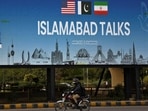A man rides his motorbike past a billboard installed alongside a road as Pakistan prepares to host the US and Iran for peace talks, in Islamabad.