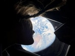 NASA astronaut and Artemis II mission specialist Christina Koch peers out of one of the Orion spacecraft's main cabin windows, looking back at Earth.