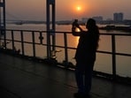 A tourist from Delhi take photos of a setting sun from a bridge on Hooghly River, in Kolkata