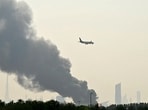 An Emirates aircraft flies past plumes of smoke from an ongoing fire near Dubai International Airport in Dubai on March 16