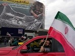 A man flashes a victory sign as he carries an Iranian flag in front of an anti-US billboard depicting the American aircrafts into the Iranian armed forces fishing net with signs that read in Farsi: "The Strait of Hormuz will remain closed, 
