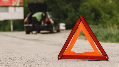 Driver putting warning triangle on asphalt road. Emergency stop concept.