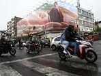 People ride motorcycles near a billboard featuring an image of Iran's new Supreme Leader Mojtaba Khamenei. 
