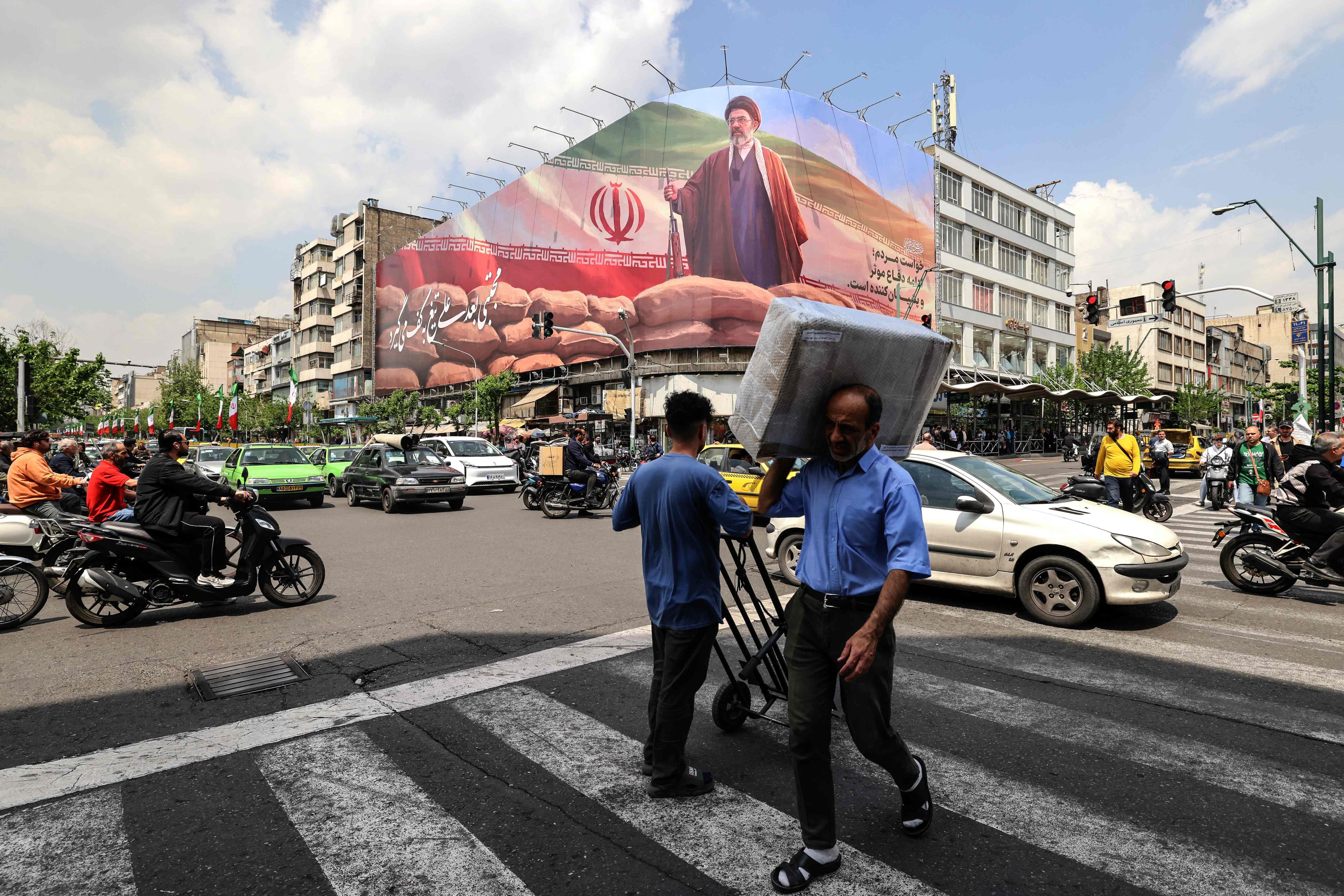 A man carrying a parcel on his shoulder walks past a large billboard depicting Iran's Supreme Leader Ayatollah Mojtaba Khamenei on a street in Tehran on April 20 (AFP) A man carrying a parcel on his shoulder walks past a large billboard depicting Iran's Supreme Leader Ayatollah Mojtaba Khamenei on a street in Tehran on April 20 (AFP)
