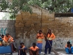 A group of Sindh Solid Waste Management Board (SSWMB) workers with dustbins and brooms, take shelter under a tree in Karachi.