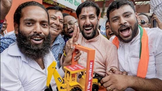 BJP supporters show a bulldozer model as they celebrate the party’s West Bengal win, in Lucknow on Monday. (PTI PHOTO)