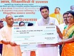 Chief minister Yogi Adityanath hands over a cheque of <span class='webrupee'>₹</span>18,000 to a Shiksha Mitra, during an event in Gorakhpur on Tuesday. (ANI)