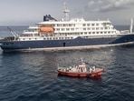 An aerial view of an ambulance boat carrying crew members wearing hazmat suits as they approach the pilot door on the starboard side of the cruise ship MV Hondius