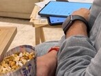 In the image, Goenka appears seated indoors, looking at a tablet while snacking on jhalmuri. 