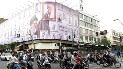 TOPSHOT - Iranians drive past a huge billboard carrying the image of the late Iranian supreme leader Ayatollah Ali Khamenei, killed in February 2026 in a military attack by the US and Israel on Iran. (AFP)