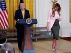 President Donald Trump stands at the podium as first lady Melania Trump exits the stage during a Mother's Day event for members of the military, May 6, in the East Room of the White House.