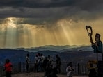 People gather at a viewpoint as clouds hover and sun rays pierce through them, in Shimla, on Sunday. (PTI)