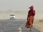 A woman covers her face while walking along a road amid dusty winds and scorching heat during a heatwave, in Prayagraj. (PTI)