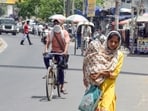 A woman covering herself and a child in her arms with a stole, walks on a road amid the scorching sun and heatwaves, in Jalandhar on Wednesday. (ANI)