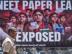 A police official passes by a poster during a protest staged by Youth Congress members over the alleged irregularities in the NEET-UG medical entrance exam