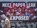 A police official passes by a poster during a protest staged by Youth Congress members over the alleged irregularities in the NEET-UG medical entrance exam
