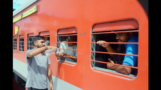 A man quenches the thirst of a passenger with a water bottle on a train during a hot summer day at the Patiala railway station on Sunday. (ANI)