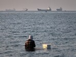 US-Iran war highlights: A person sits in shallow water as cargo and commercial vessels are anchored in the Strait of Hormuz off Bandar Abbas, Iran.