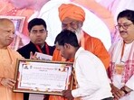 Chief minister Yogi Adityanath distributes an appointment letter to a beneficiary during the inauguration and foundation stone-laying ceremony of 101 development projects, in Unnao on Thursday. (@myogiadityanath X/ANI Photo)
