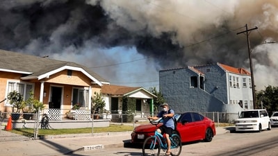 LOS ANGELES, CALIFORNIA - JUNE 20: A person rides a bicycle as a massive warehouse fire at a cold storage facility continues to burn and spread smoke around the city on June 20, 2026 in Los Angeles, California. (Photo by MARIO TAMA / GETTY IMAGES NORTH AMERICA / Getty Images via AFP) (Getty Images via AFP)