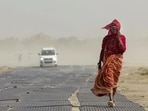 A woman covers her face while walking along a road amid dusty winds and scorching heat during a heatwave. (PTI)