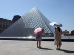 Tourists protecting themselves from the sun with umbrellas stand in front of the glass Pyramid of the Louvre museum as the museum closes early due to the heatwave as temperatures rise in Paris, France.